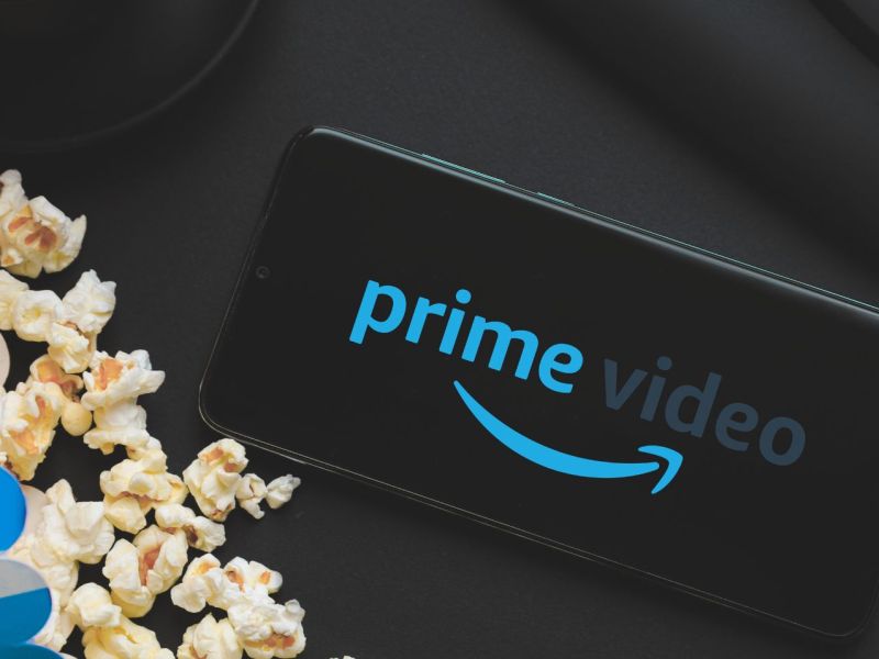 Logo von Amazon Prime Video auf einem Handy, daneben eine Tüte Popcorn.