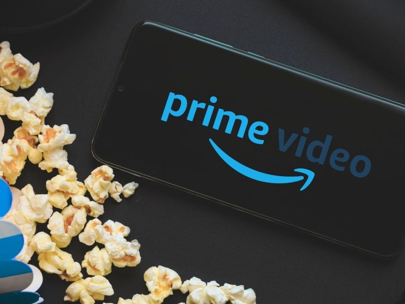 Logo von Amazon Prime Video auf einem Handy, daneben eine Tüte Popcorn.