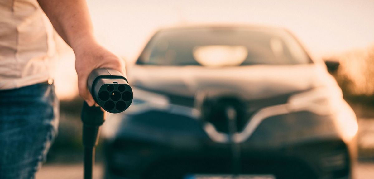 Person mit Ladestecker eines Elektroautos in der Hand