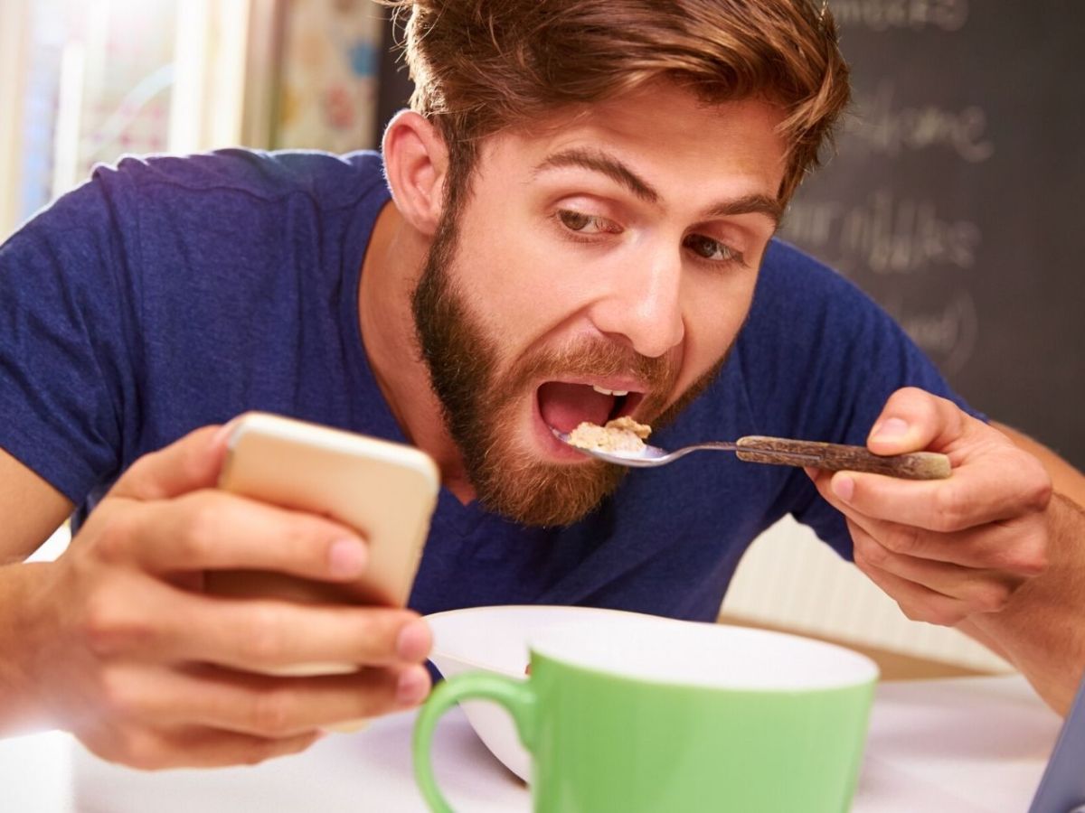 Mann isst während er sein Handy hält