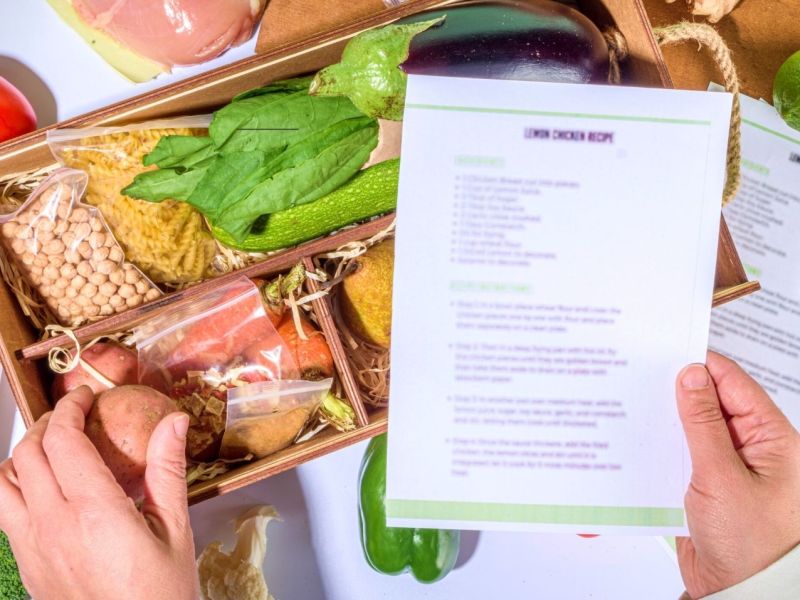 Person hält Rezept über eine Kochbox