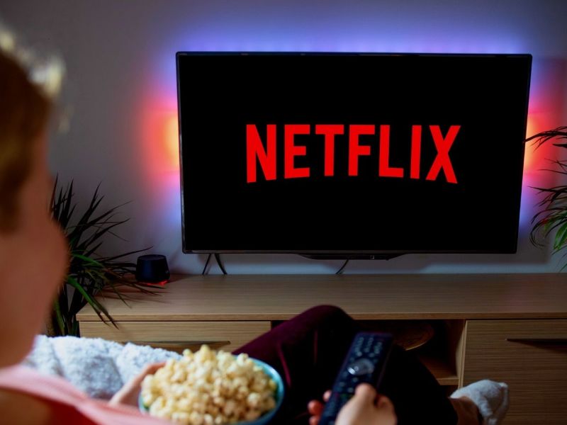 Frau sitzt mit einer Schüssel Popcorn vor dem TV und schaut Netflix.