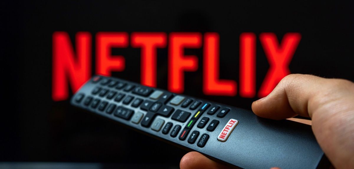 Netflix-Logo auf einem TV, davor eine Person mit einer Fernbedienung.