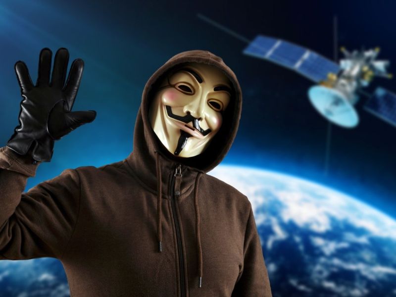 Person mit Guy Fawkes-Maske vor einem Satelliten