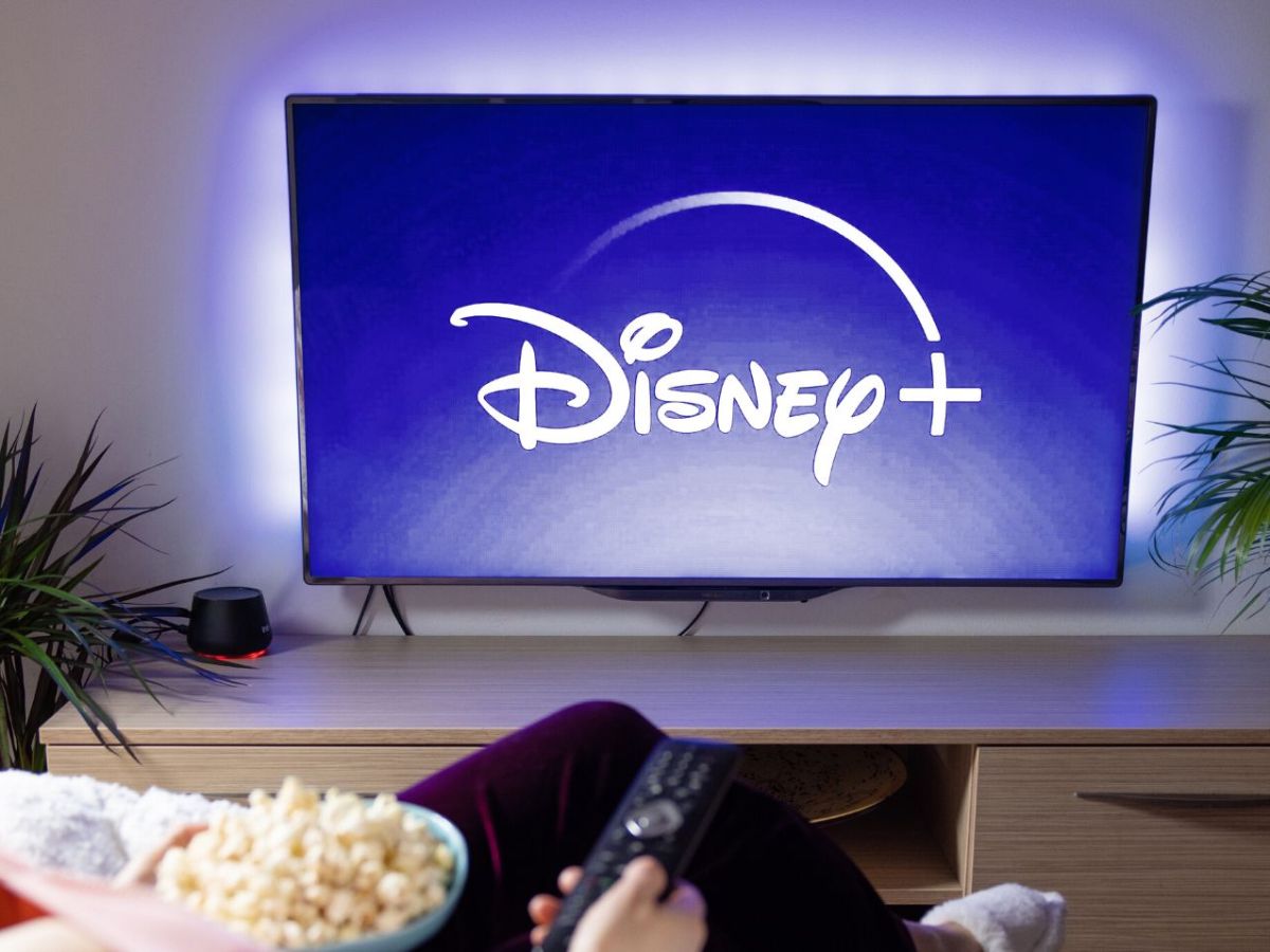 Disney Plus-Logo auf einem TV, davor eine Frau mit Popcorn.