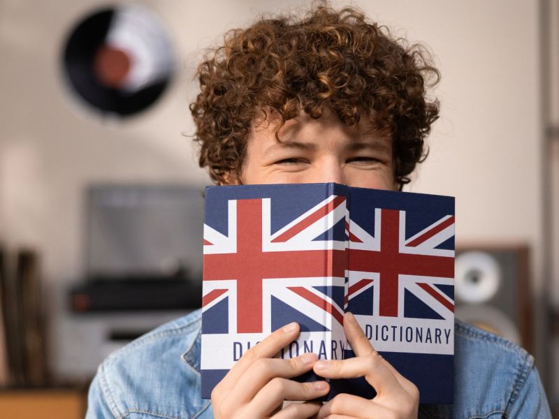 Junger Mann mit Englisch-Wörterbuch vor dem Gesicht.