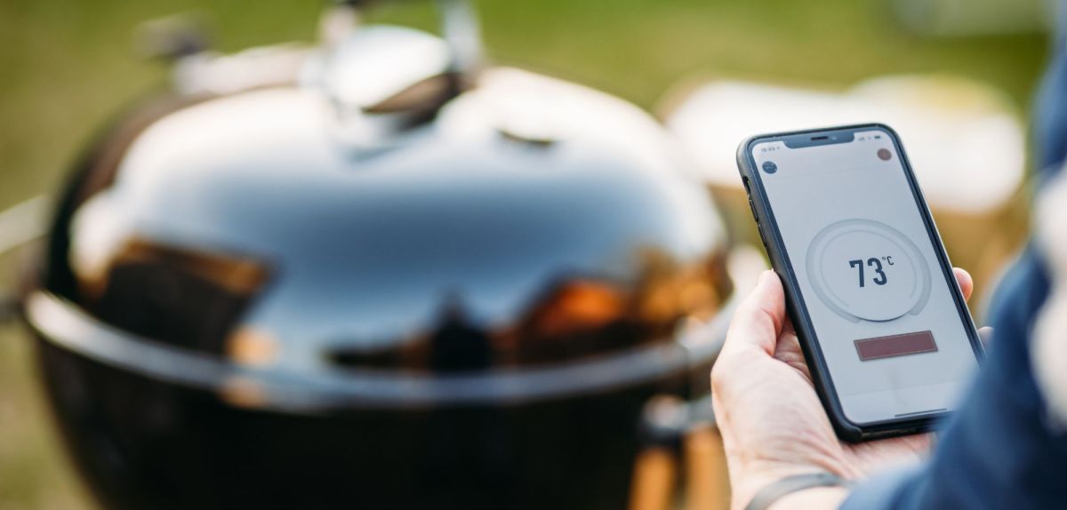 Person mit Smartphone in der Hand vor einem Grill