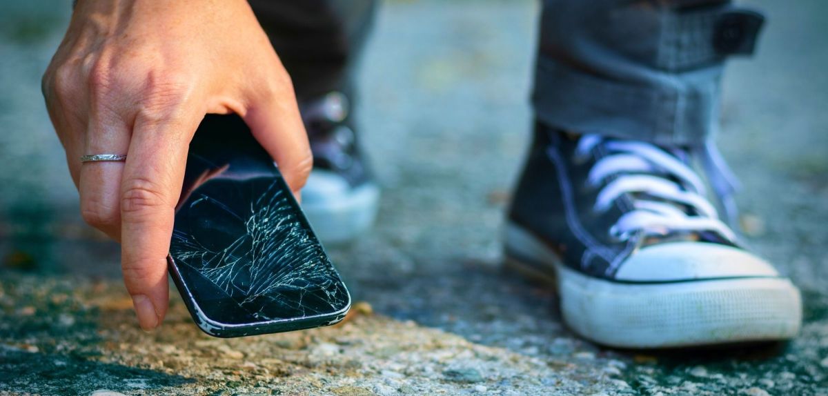 Person hebt kaputtes Smartphone vom Boden auf