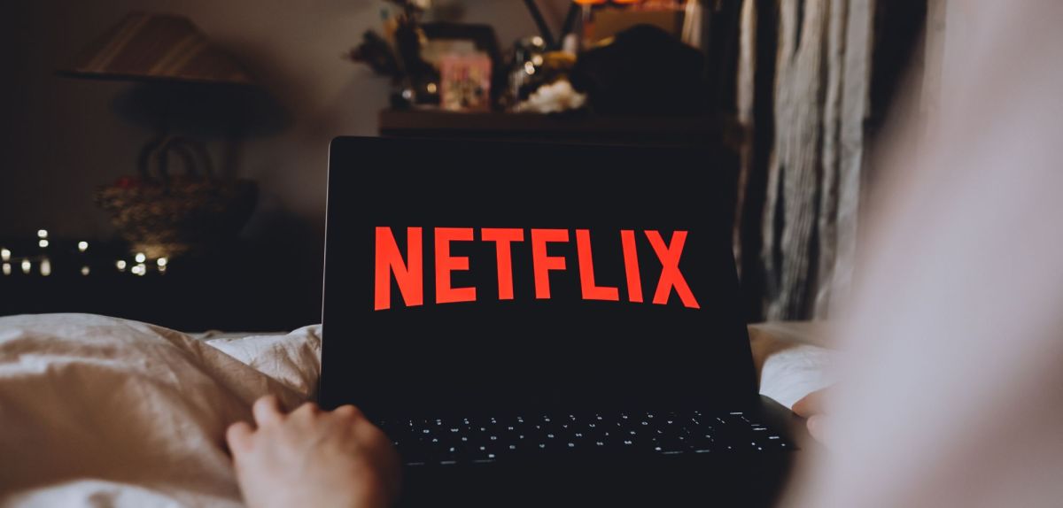 Person mit Laptop auf dem Schoß, Netflix-Logo auf dem Display.