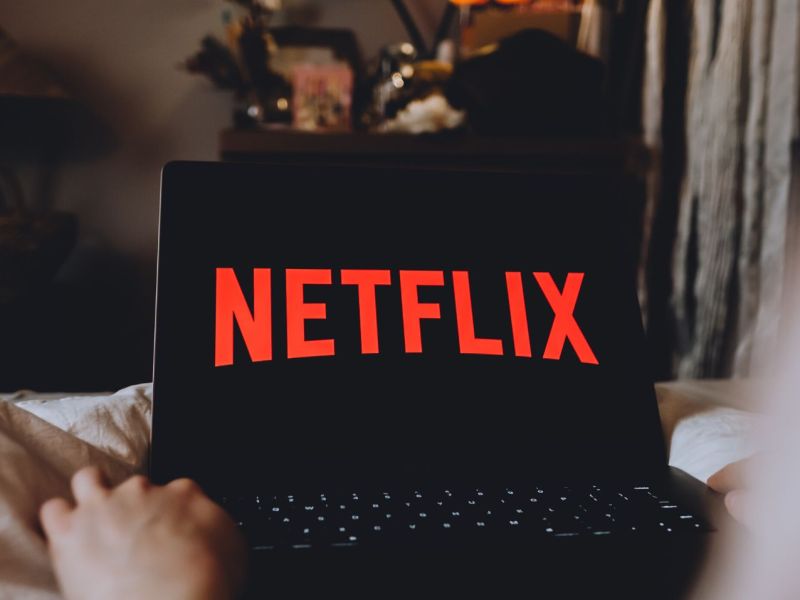 Person mit Laptop auf dem Schoß, Netflix-Logo auf dem Display.