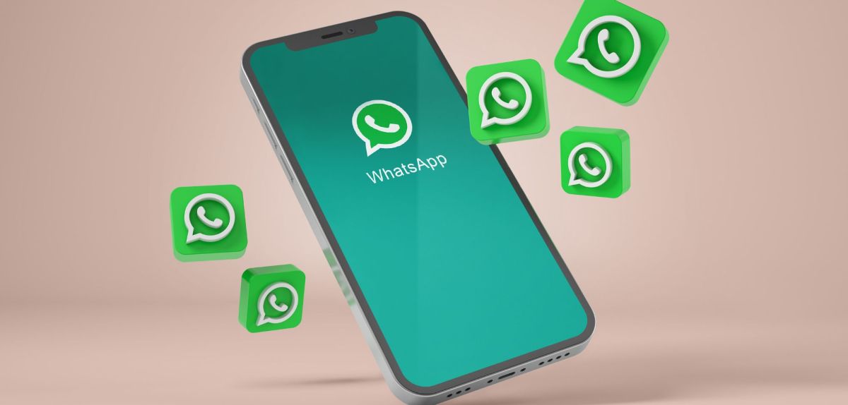 WhatsApp-Logo auf einem Handy, drumherum fliegen mehrere WhatsApp-Symbole.