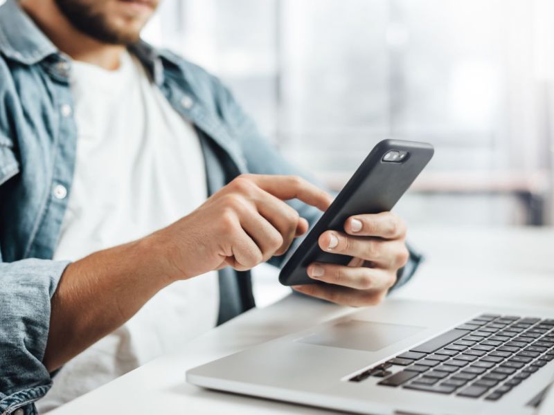 Mann mit Handy und Laptop an einem Schreibtisch