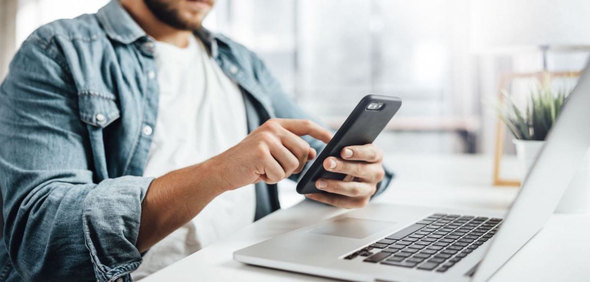 Mann mit Handy und Laptop an einem Schreibtisch