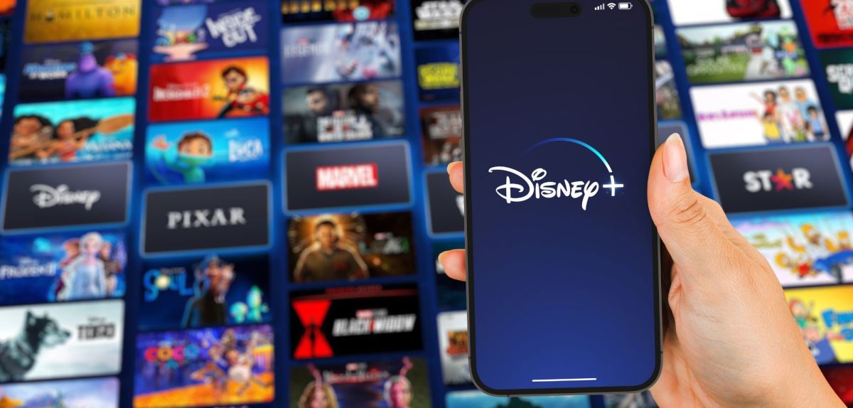 Disney Plus-Logo auf einem Handy, dahinter zahlreiche Film- und Serienkacheln.