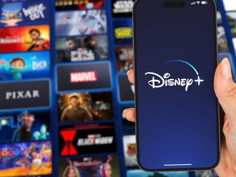 Disney Plus-Logo auf einem Handy, dahinter zahlreiche Film- und Serienkacheln.
