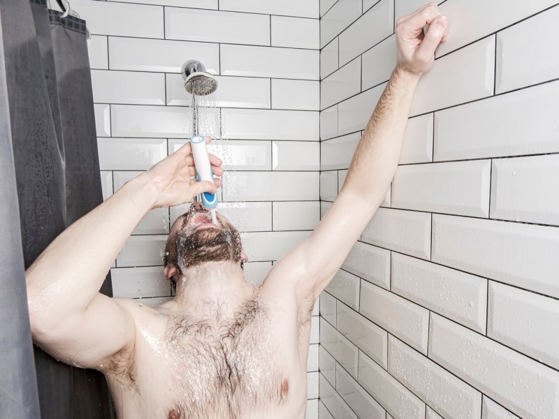 Mann unter der Dusche mit Zahnbürste
