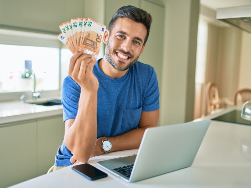 Mann mit Geld in der Hand am Laptop