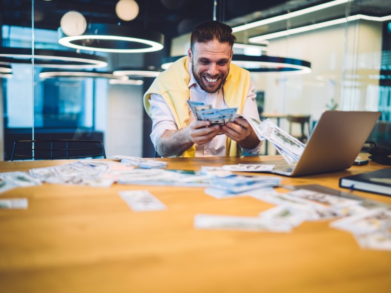 Mann mit Geld in der Hand am Laptop