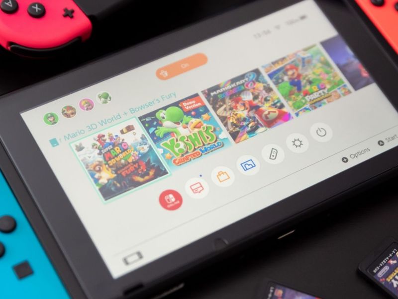 Eine eingeschaltete Nintendo Switch, auf dem Display sind Kacheln für verschiedene Spiele zu sehen.