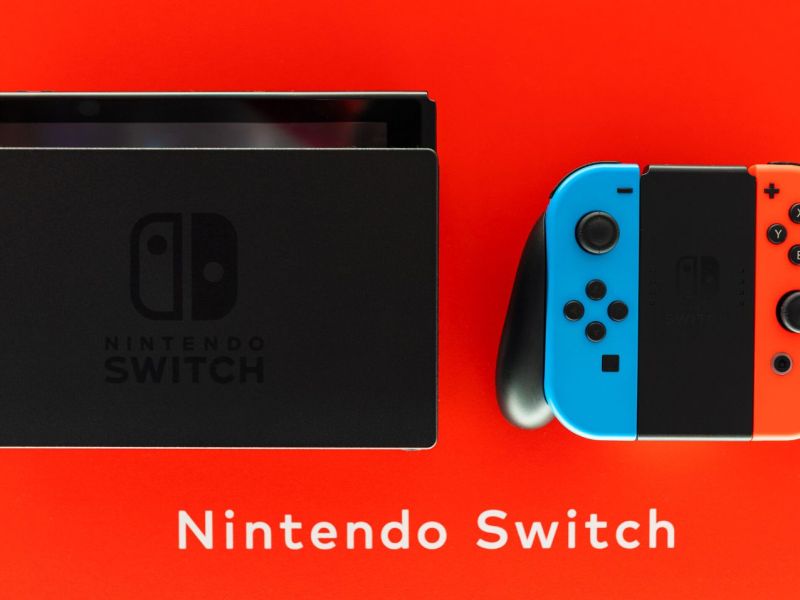 Eine Nintendo Switch mit Joycon-Controllern und Dockingstation vor rotem Hintergrund.