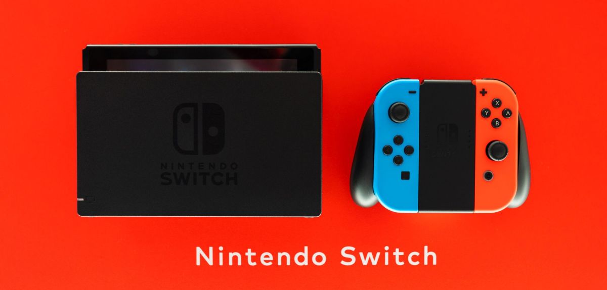 Eine Nintendo Switch mit Joycon-Controllern und Dockingstation vor rotem Hintergrund.