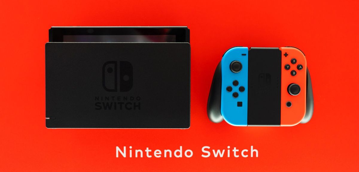 Eine Nintendo Switch mit Joycon-Controllern und Dockingstation vor rotem Hintergrund.