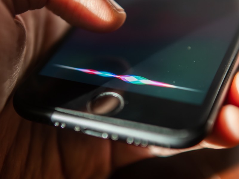 Person hält den Finger über ein Handy, dessen Sprachassistent aktiv ist.