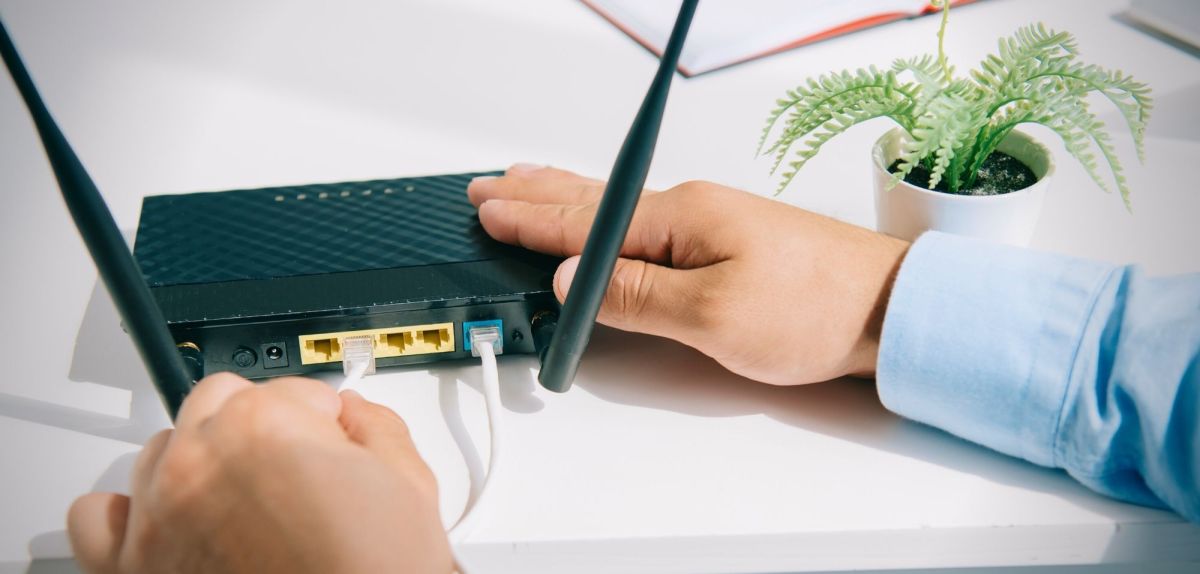 Person steckt Kabel in einen WLAN-Router