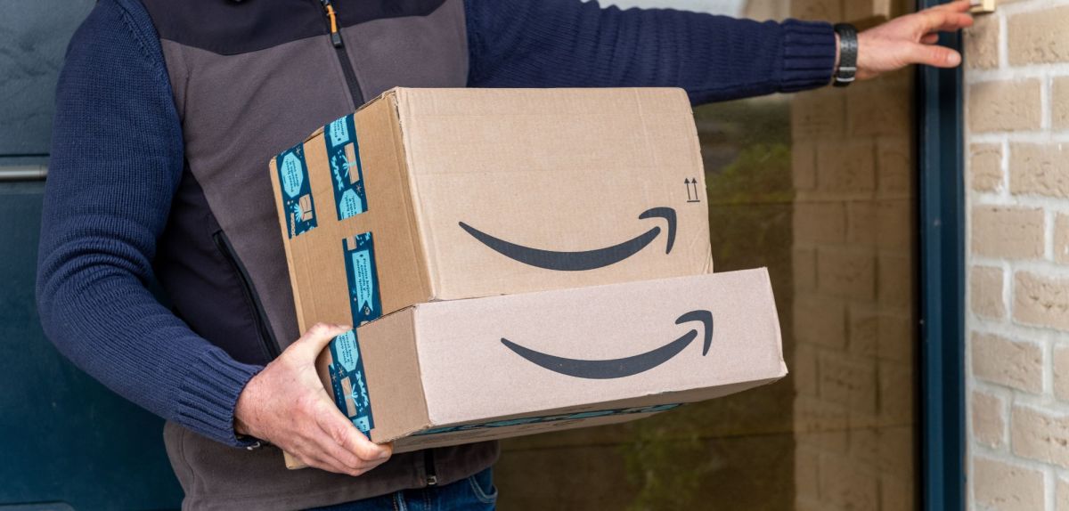 Bote mit einem Stapel Amazon-Pakete klingelt an einer HaustÃ¼r.