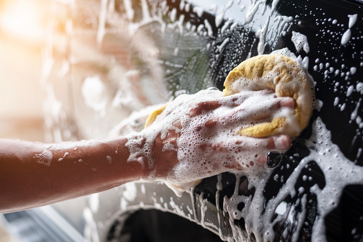 Person wäscht Auto mit Schwamm und Seife