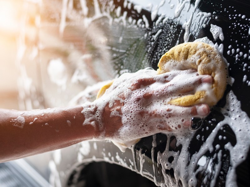 Person wäscht Auto mit Schwamm und Seife