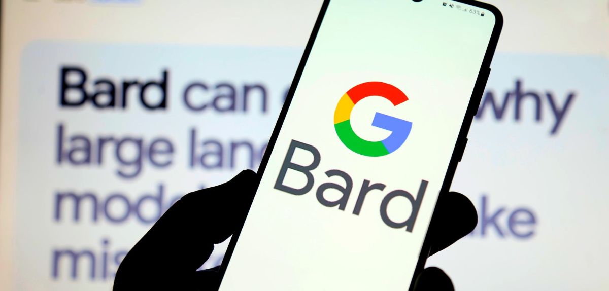 Logo für Google Bard auf einem Handy, dahinter Text auf einem Bildschirm.