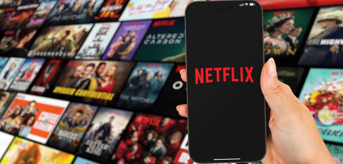 Netflix Logo auf dem Handy im Hintergrund Titelbilder von Filmen und Serien