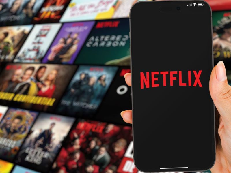Netflix Logo auf dem Handy im Hintergrund Titelbilder von Filmen und Serien