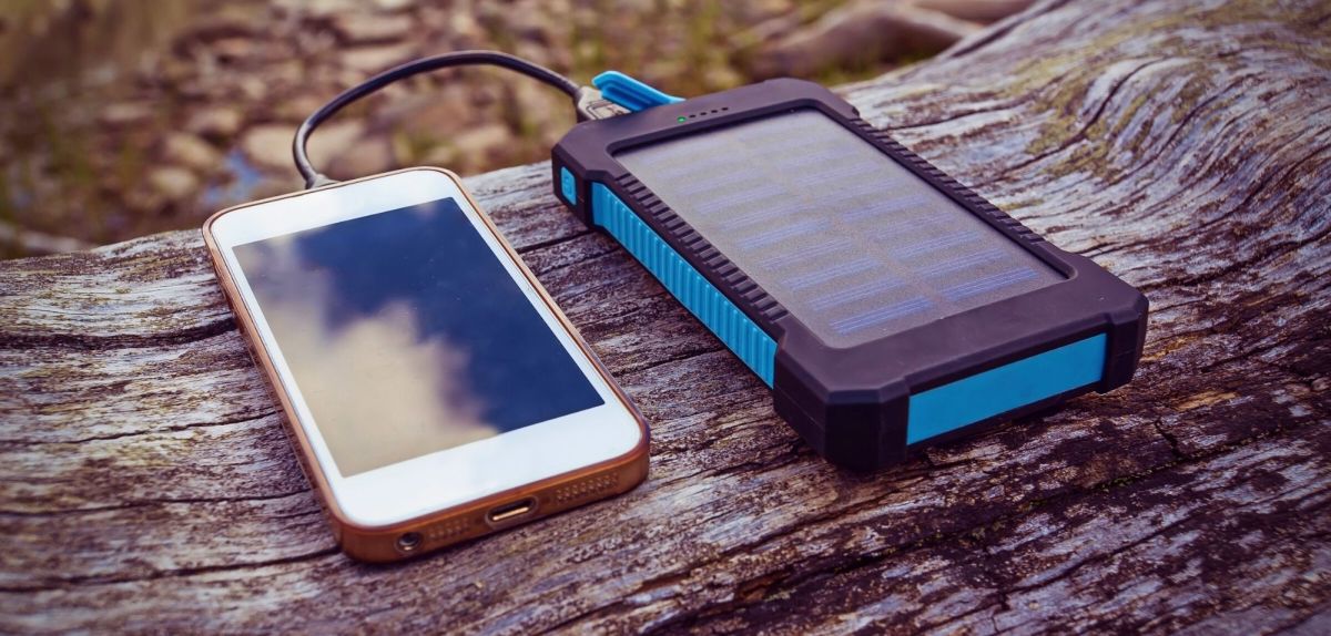 Solar-Powerbank mit Smartphone auf Baumstamm.