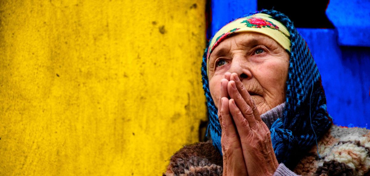 Frau betet vor einer gelb-blauen Wand