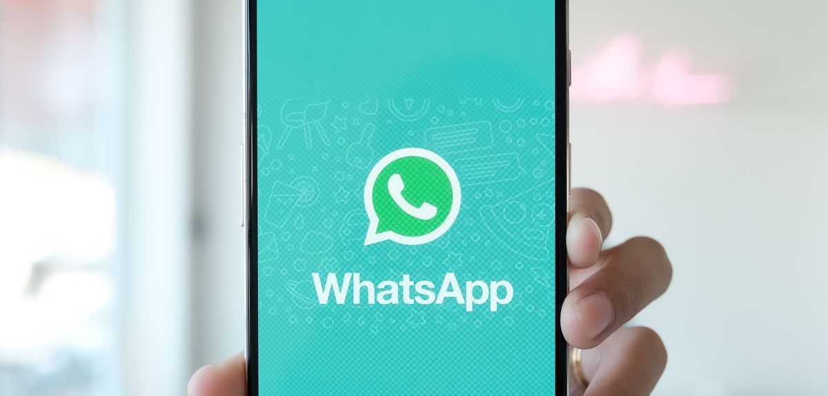 Person hält Handy mit WhatsApp-Logo in die Kamera.