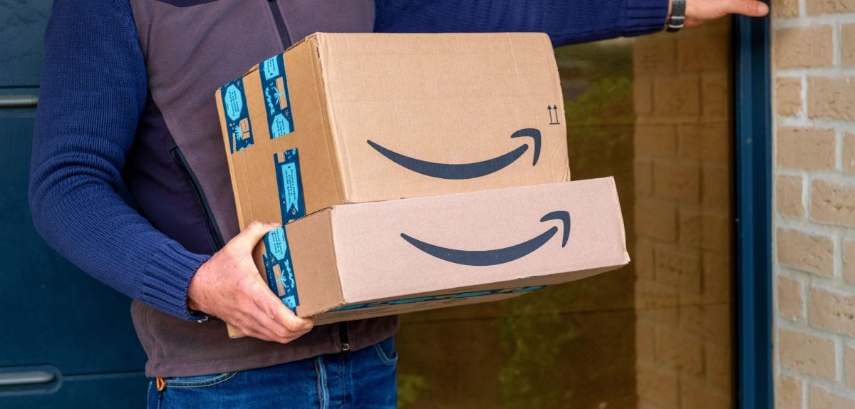 Mann hält Stapel Pakete von Amazon in der Hand.