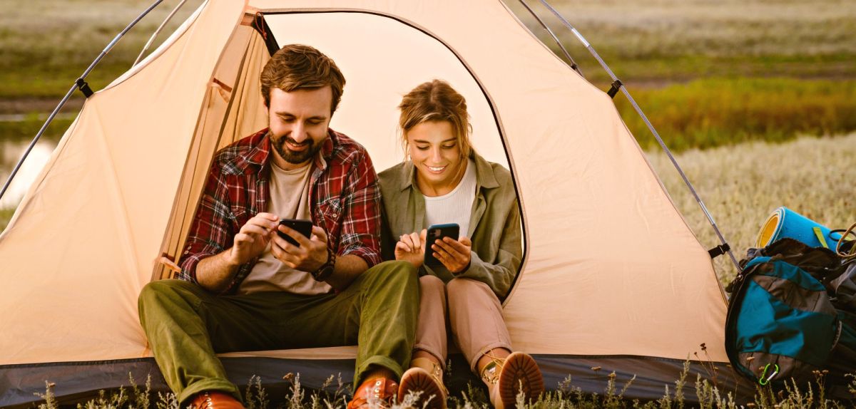 Mann und Frau sitzen mit Smartphone im Zelt