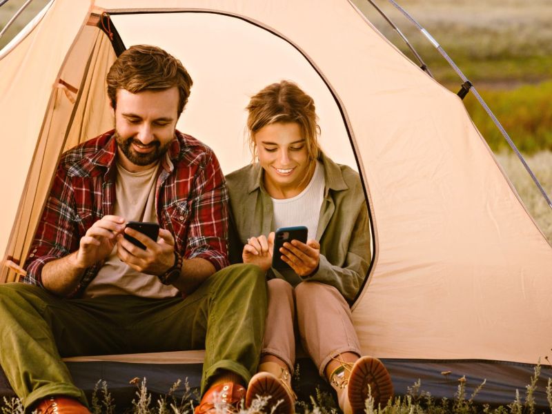 Mann und Frau sitzen mit Smartphone im Zelt
