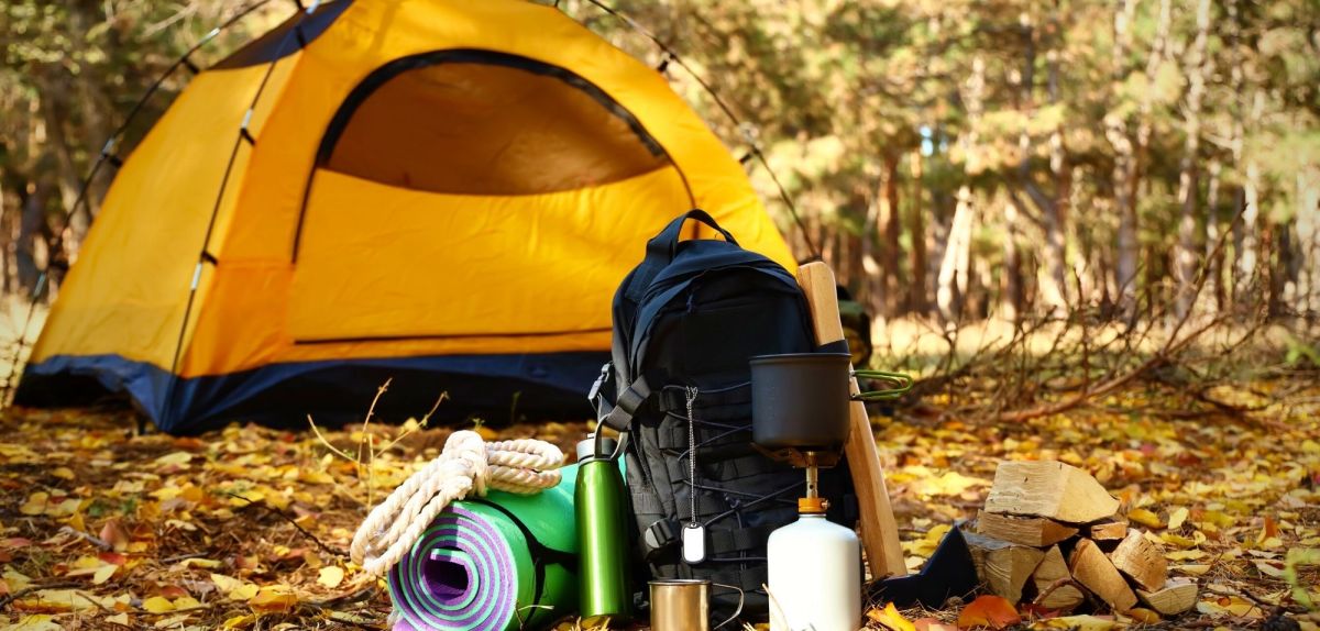 Ein Zelt im Wald, davor Camping-Zubehör.