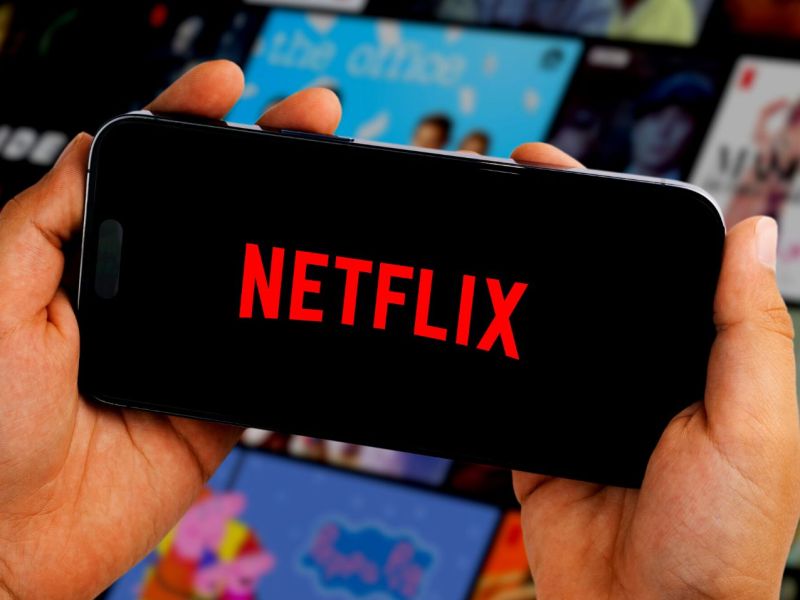 Person hält Handy mit Netflix-Logo in Händen vor einer Vielzahl an Streaming-Kacheln.