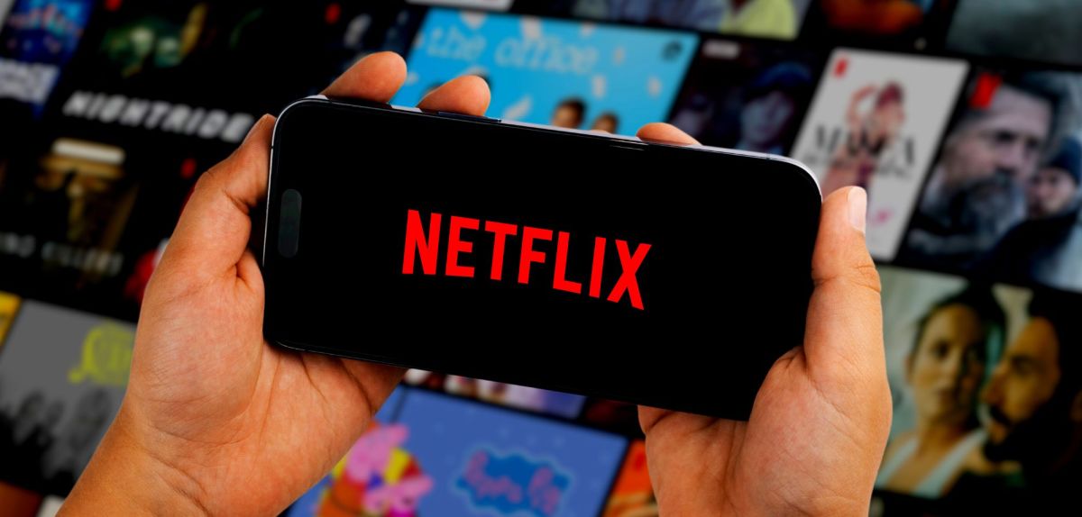 Person hält Handy mit Netflix-Logo in Händen vor einer Vielzahl an Streaming-Kacheln.