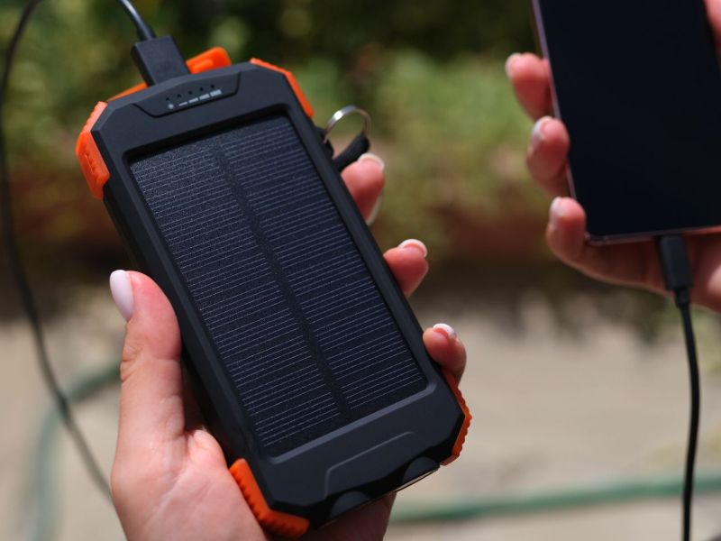 Zwei Hände halten ein Smartphone und eine Solar-Powerbank