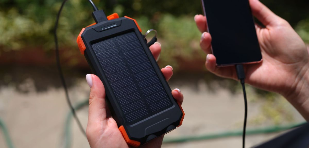 Zwei Hände halten ein Smartphone und eine Solar-Powerbank
