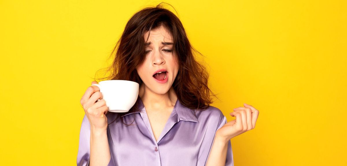 Frau gähnt mit einer Tasse Kaffee in der Hand.