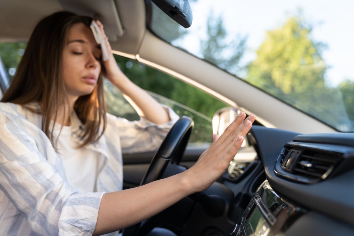 Frau hält im Auto die Hand vor die Klimaanlage