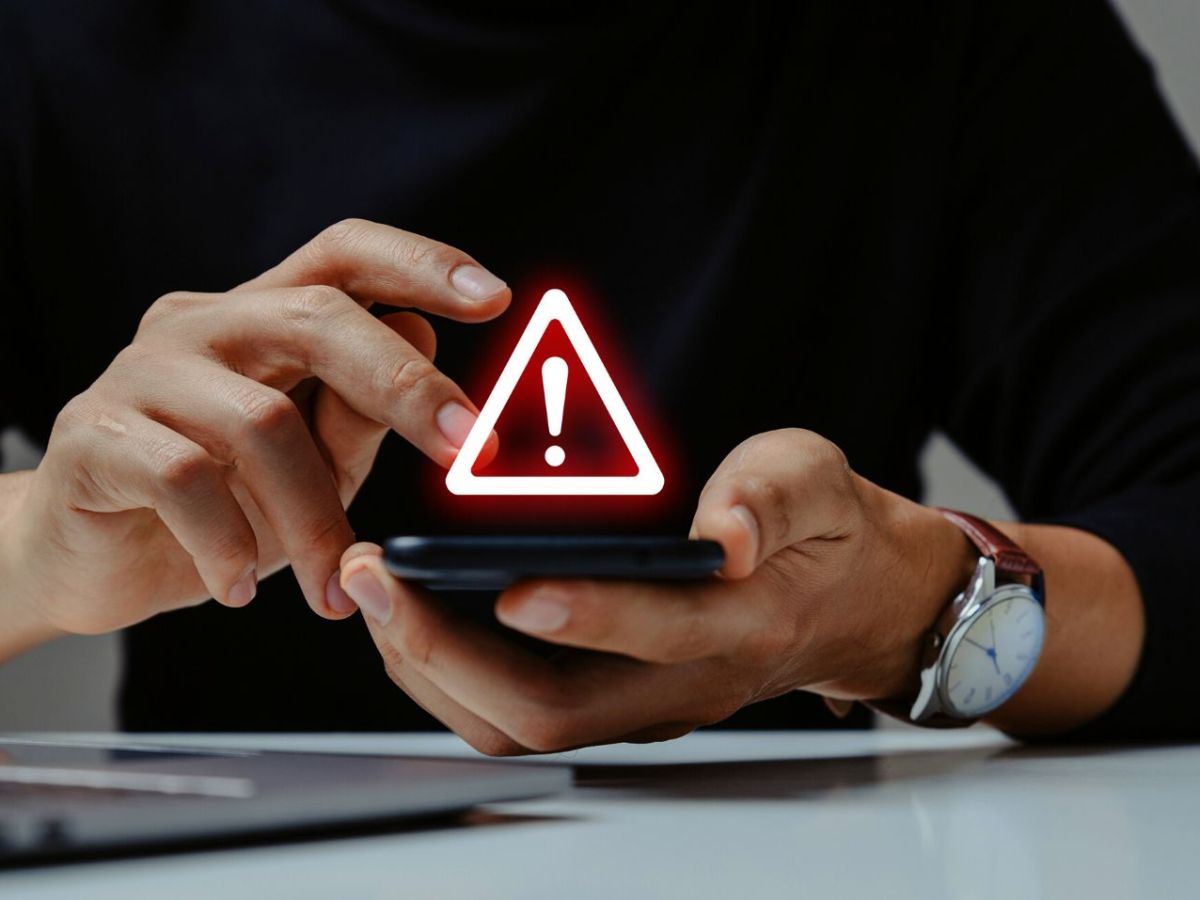 Person hält Handy in Händen, darüber leuchtet ein Warnsignal auf.