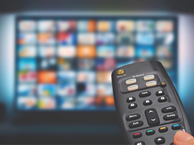 Person richtet Fernbedienung auf Fernseher mit Streaming-Kacheln.