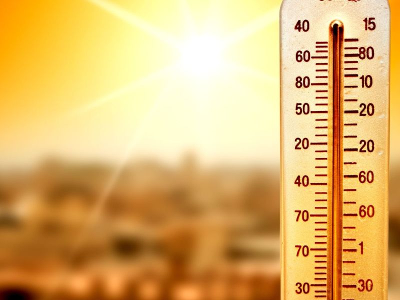 Ein Thermometer zeigt hohe Temperaturen an, im Hintergrund scheint die Sonne auf eine Stadt.